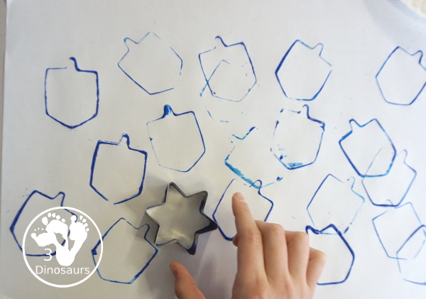  Hanukkah Stamping Painting with Cookie Cutters is a great Hanukkah craft you can do with different ages. And a fun mix of Hanukkah themes you can find in the cookie cutters.