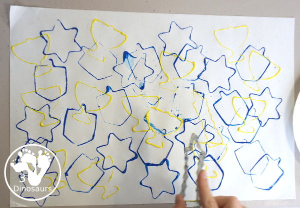  Hanukkah Stamping Painting with Cookie Cutters is a great Hanukkah craft you can do with different ages. And a fun mix of Hanukkah themes you can find in the cookie cutters.