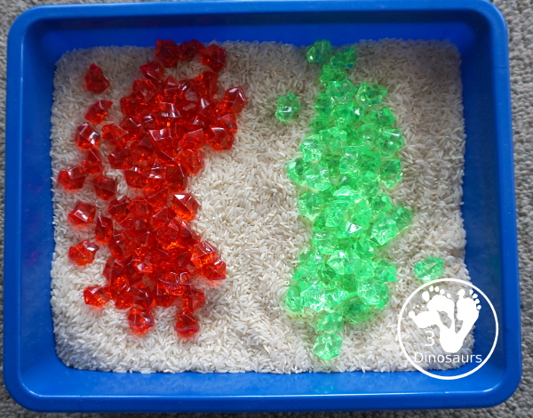 Christmas Red & Green Sensory Bin with red rocks and green rocks with a rice filler in a small bin that you can use for small sensory bin exploring with kids in preschool, preK and kindergarten. - 3Dinosaurs.com