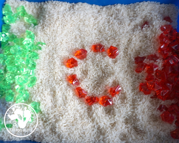 Christmas Red & Green Sensory Bin with red rocks and green rocks with a rice filler in a small bin that you can use for small sensory bin exploring with kids in preschool, preK and kindergarten. - 3Dinosaurs.com