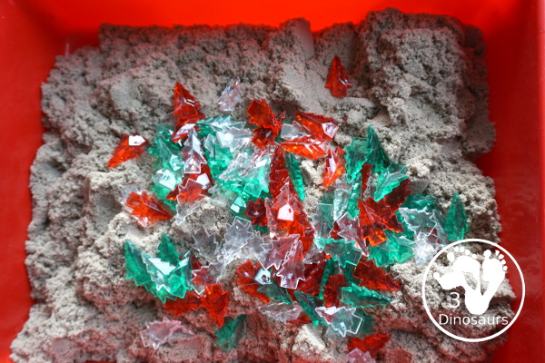 Christmas Tree & Kinetic Sand Sensory Bin - a simple sensory bin with a mix of red, green and clear evergreen trees in a kinetic sand fill for the sensory bin. This sensory bin is in a small paper bin that is great for sensory play with small groups. - 3Dinosaurs.com