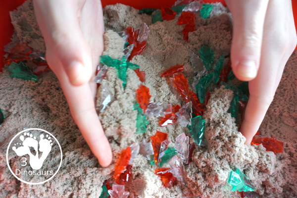 Christmas Tree & Kinetic Sand Sensory Bin - a simple sensory bin with a mix of red, green and clear evergreen trees in a kinetic sand fill for the sensory bin. This sensory bin is in a small paper bin that is great for sensory play with small groups. - 3Dinosaurs.com