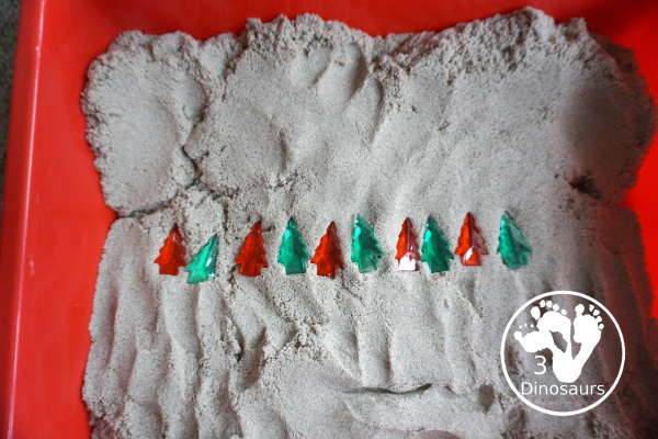 Christmas Tree & Kinetic Sand Sensory Bin - a simple sensory bin with a mix of red, green and clear evergreen trees in a kinetic sand fill for the sensory bin. This sensory bin is in a small paper bin that is great for sensory play with small groups. - 3Dinosaurs.com