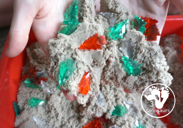 Christmas Tree & Kinetic Sand Sensory Bin - a simple sensory bin with a mix of red, green and clear evergreen trees in a kinetic sand fill for the sensory bin. This sensory bin is in a small paper bin that is great for sensory play with small groups. - 3Dinosaurs.com