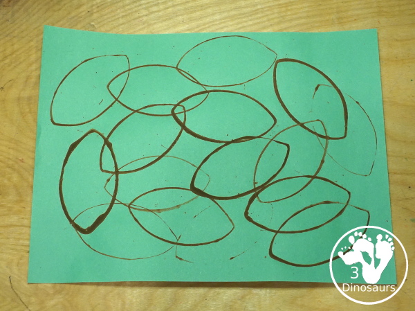 Football Stamp Painting with Cookie Cutters - You use a football shape cookie cutter to stamp brown footballs all over a green paper - 3Dinosaurs.com